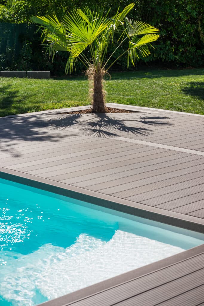 Terrasse Bois Composite Piscine & Palmier Design Palmier isolé sur terrasse composite moderne au bord d'une piscine aux eaux turquoise, ombres portées sur le bois.